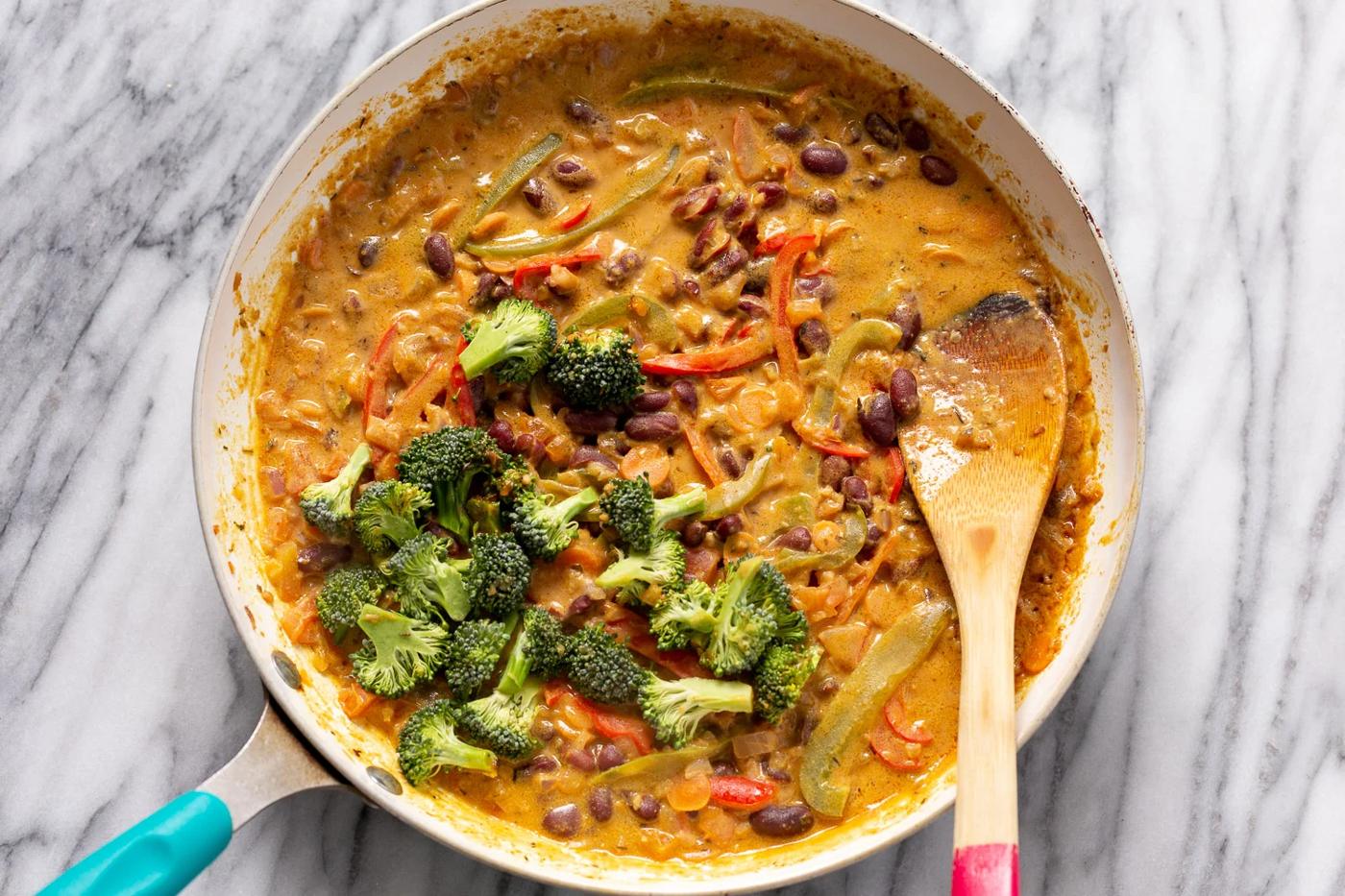 broccoli florets being stirred into a pan with creamy vegan Peanut Stew
