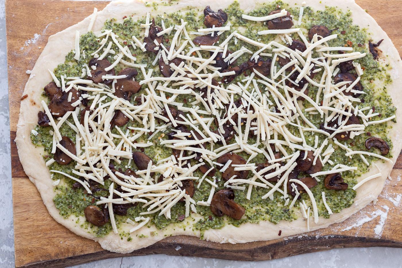 shredded vegan mozzarella being sprinkled onto pizza dough to make pesto pizza rolls