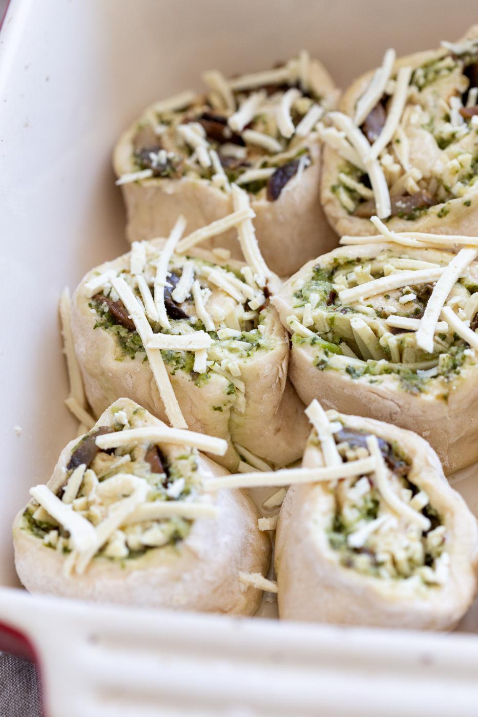 Pesto Pizza rolls unbaked in a white ceramic baking dish