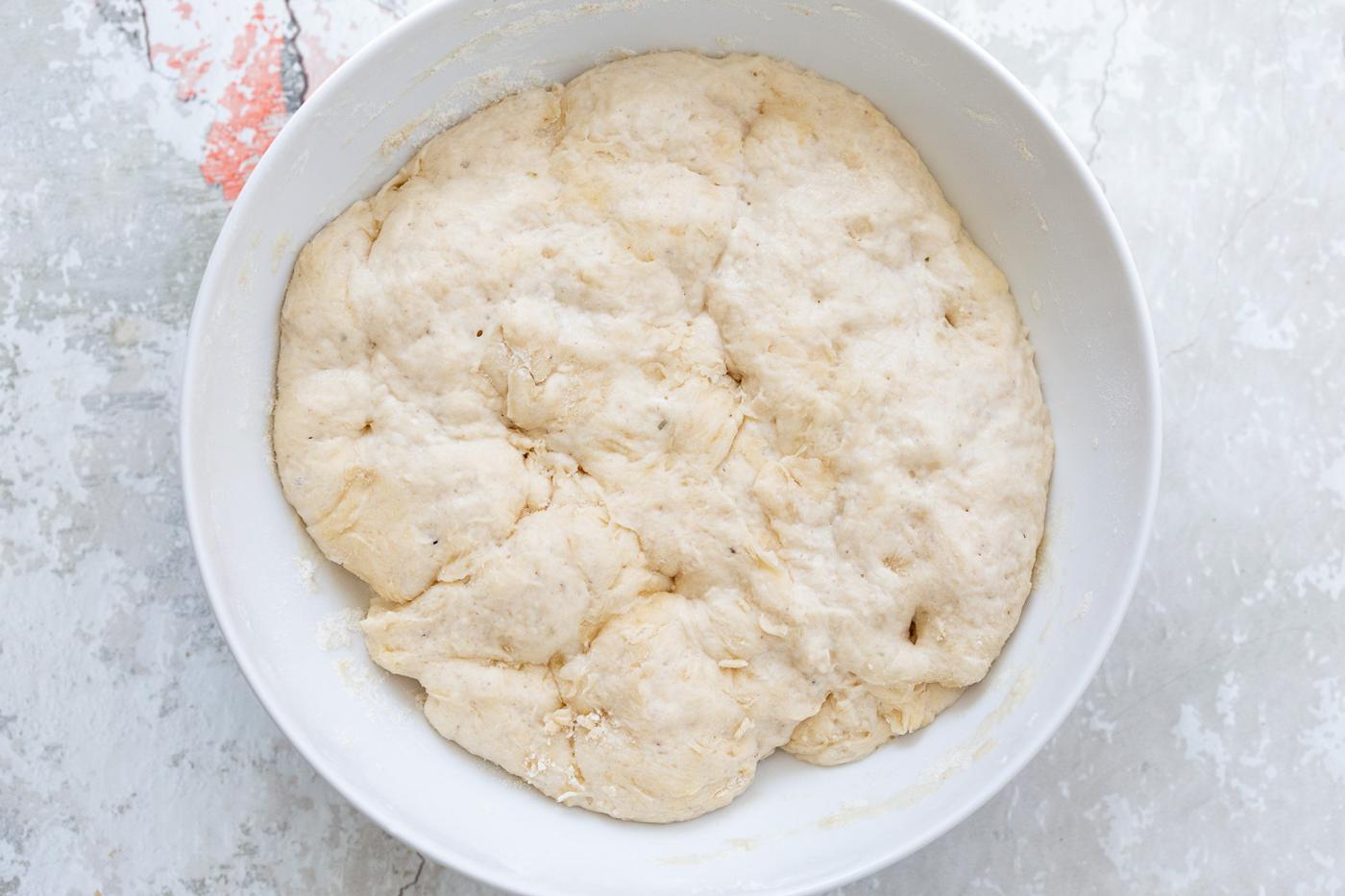 proofed pizza dough doubled in size sitting in a white bowl ready to be punched down