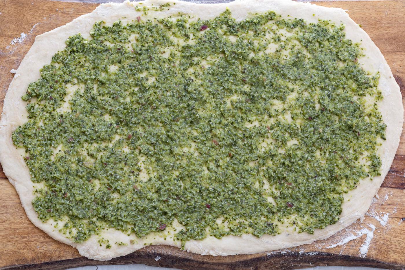 vegan pesto being spread onto rolled out pizza rolls dough