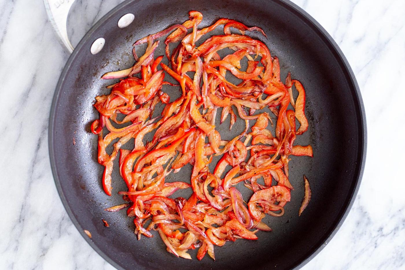 red bell peppers being sauteed in a frying pan