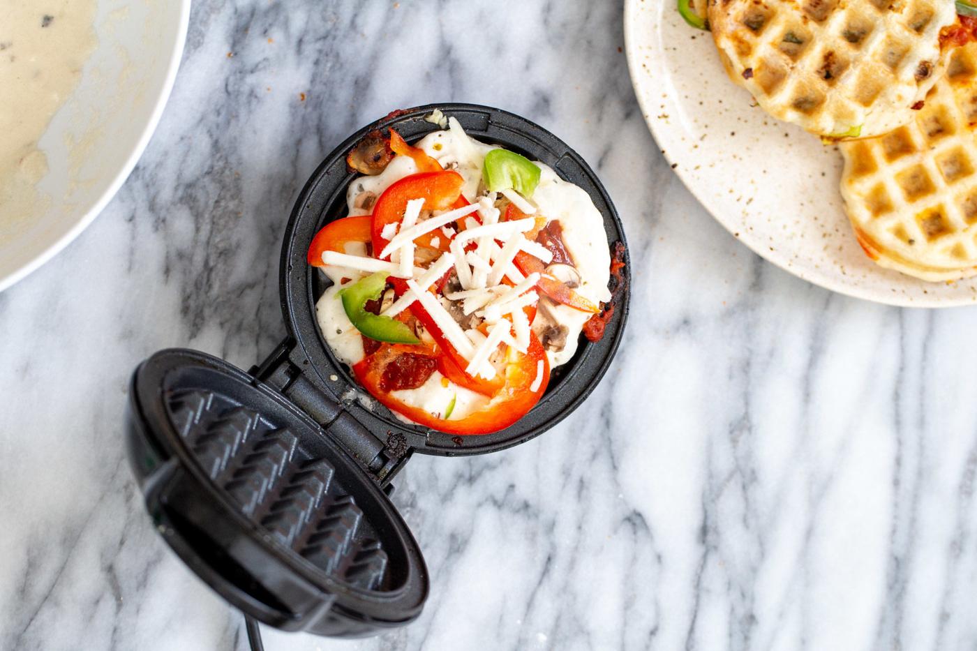 vegan pizza waffle being topped with shredded mozzarella cheese
