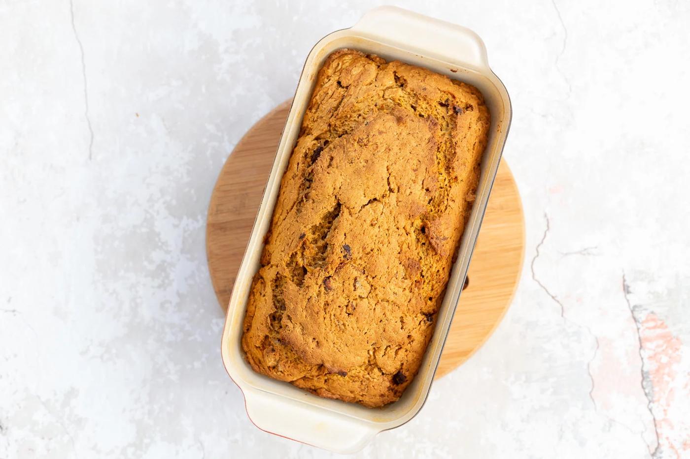 a freshly baked loaf of vegan pumpkin carrot bread cooling on a chopping board