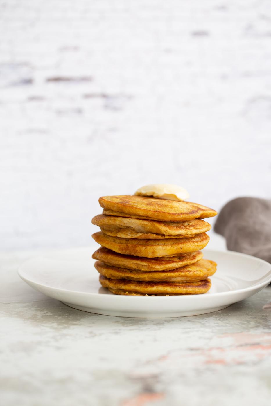 a stack of vegan pumpkin pancakes against a white brick wall