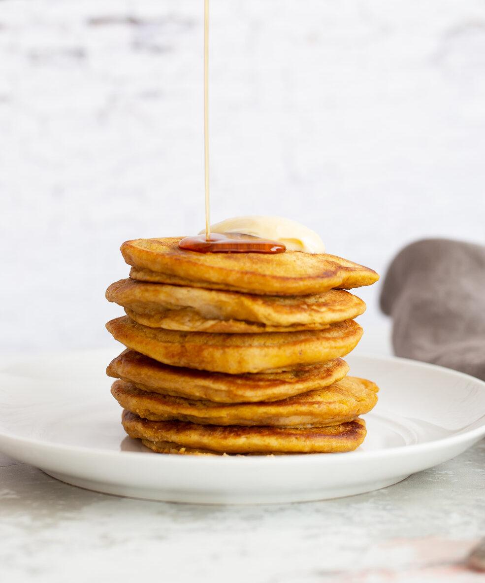 a stack of vegan pumpkin pancakes being drizzled with maple syrup