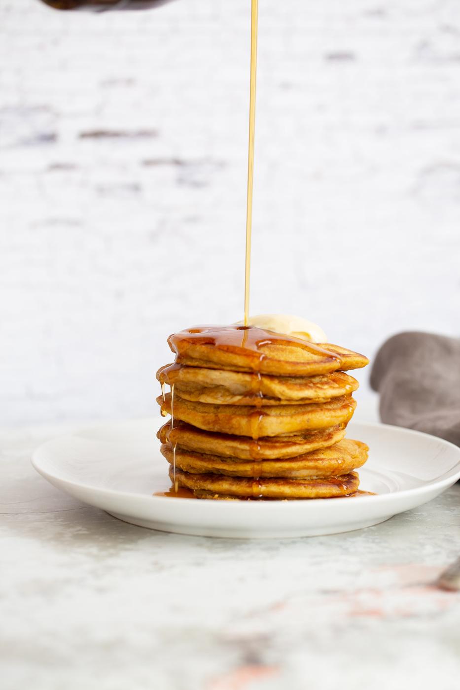 a stack of pancakes being drizzled with maple syrup