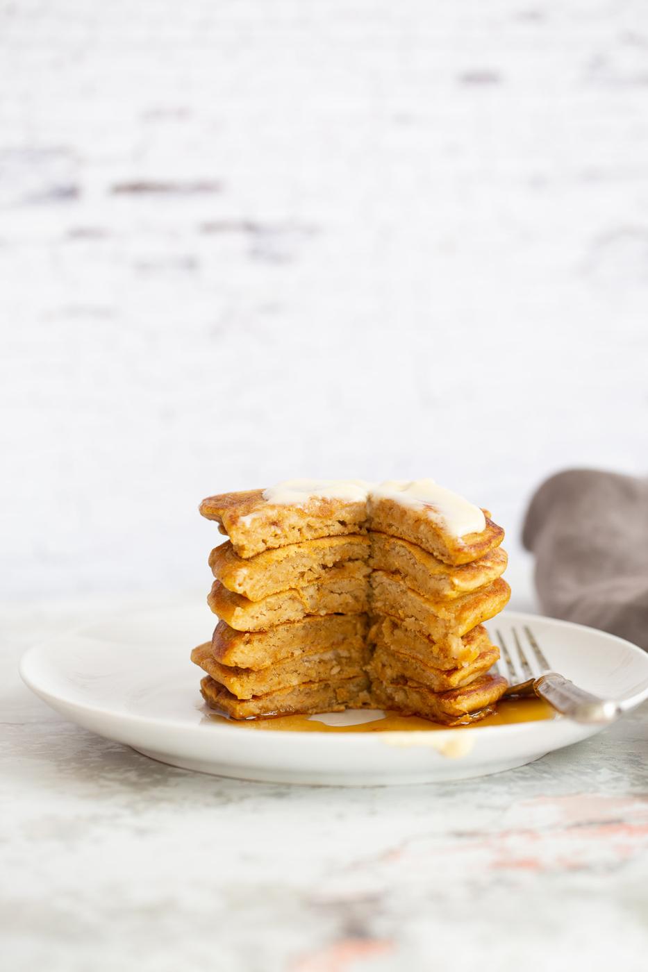 a half-eaten stack of vegan pumpkin pancakes drizzled with maple syrup