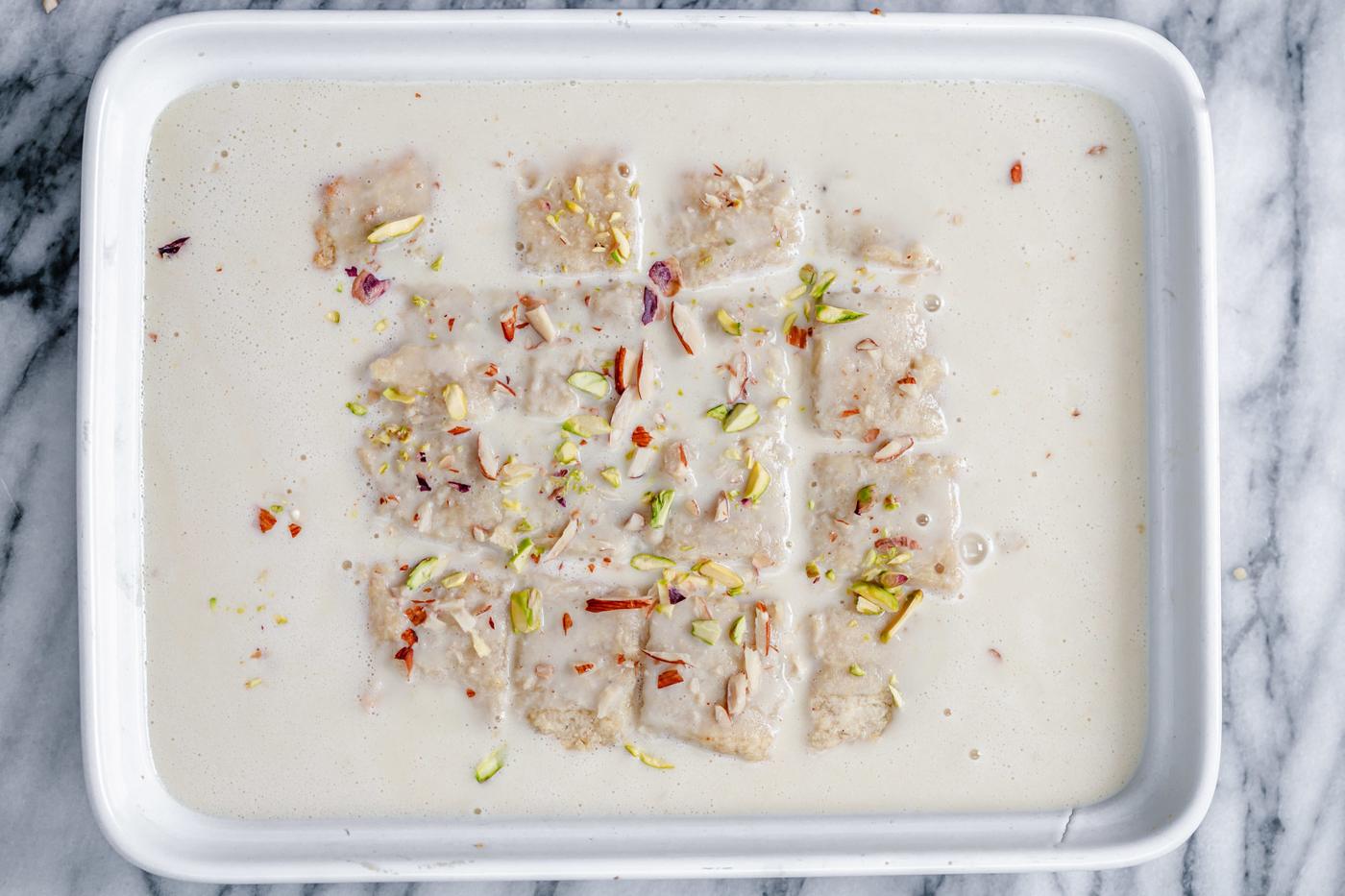 vegan rasmalai cake being immersed in vegan milk sauce