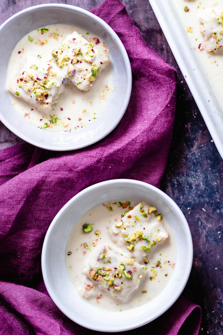 overhead shot of two bowl of vegan rasmalai cake served with vegan cashew pistachio cream sauce