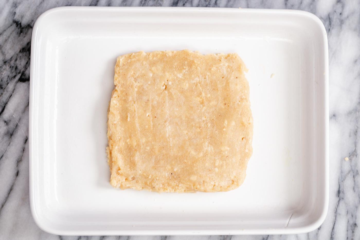 rasmalai cake batter being shaped to a square in a pan