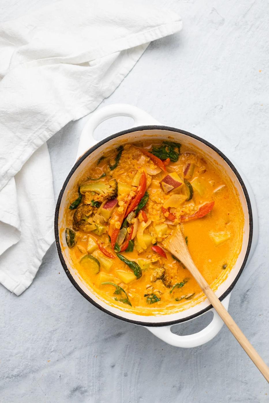overhead shot of a white ceramic pot filled with vegan red lentil sweet potato curry