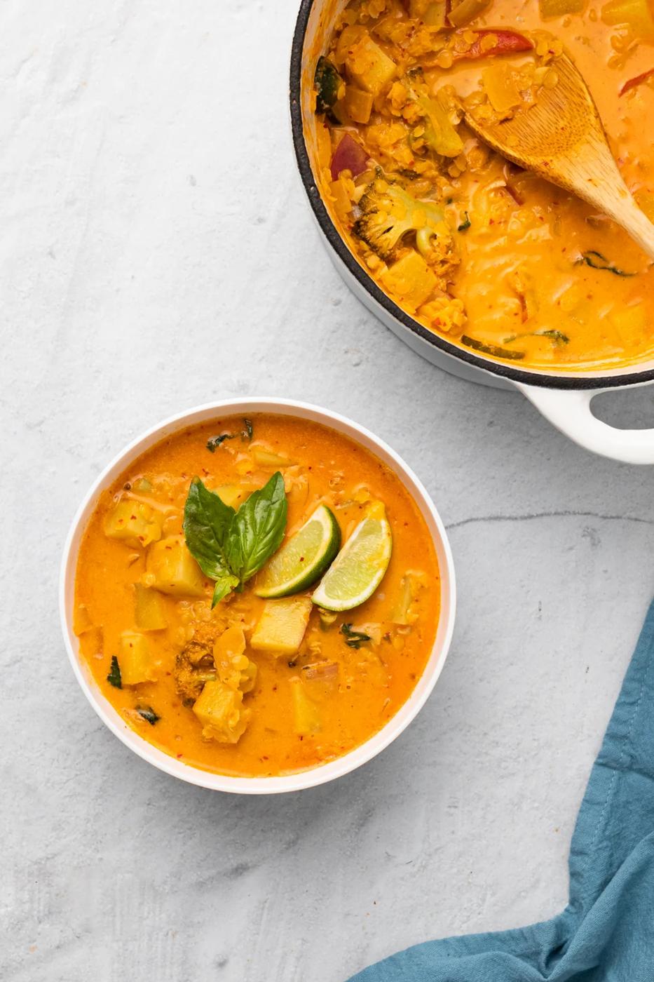 a bowl of vegan Thai sweet potato curry with red lentils next to a pot