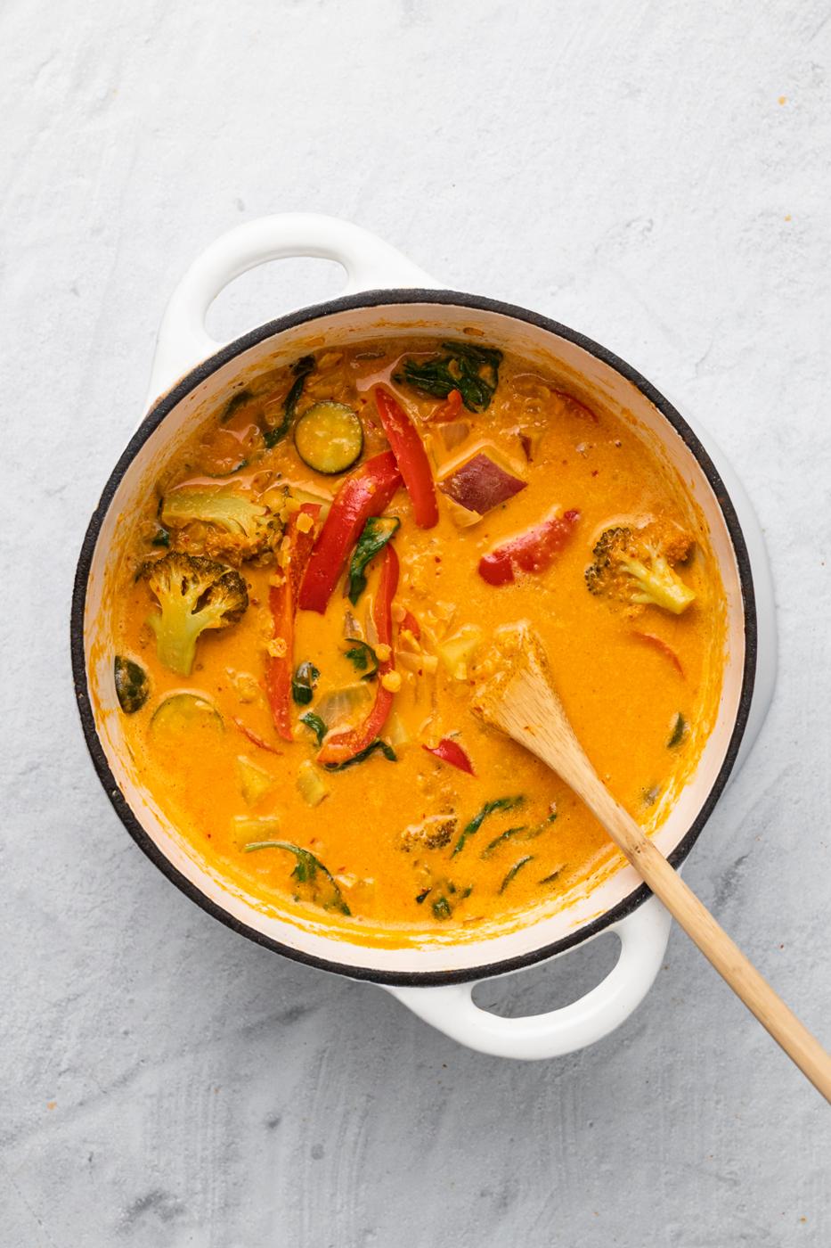 overhead shot of a pot of vegan red lentil sweet potato curry in a white pot with a wooden spoon
