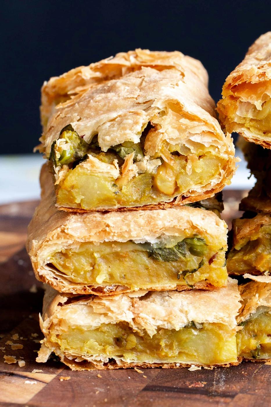 stacked pieces of vegan potato samosa pie on a wooden board