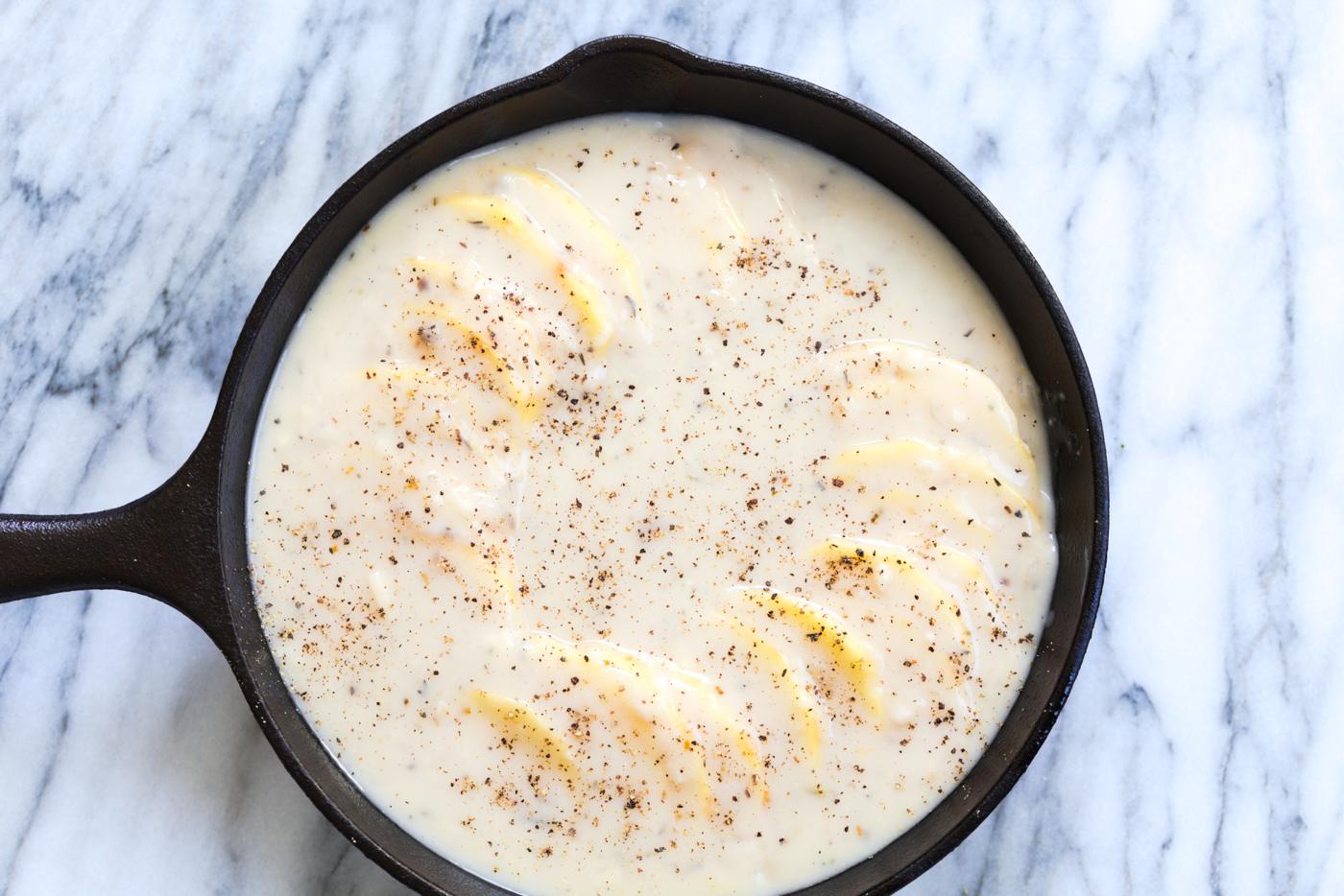 Scalloped potatotes in a Cast iron skillet ready to bake