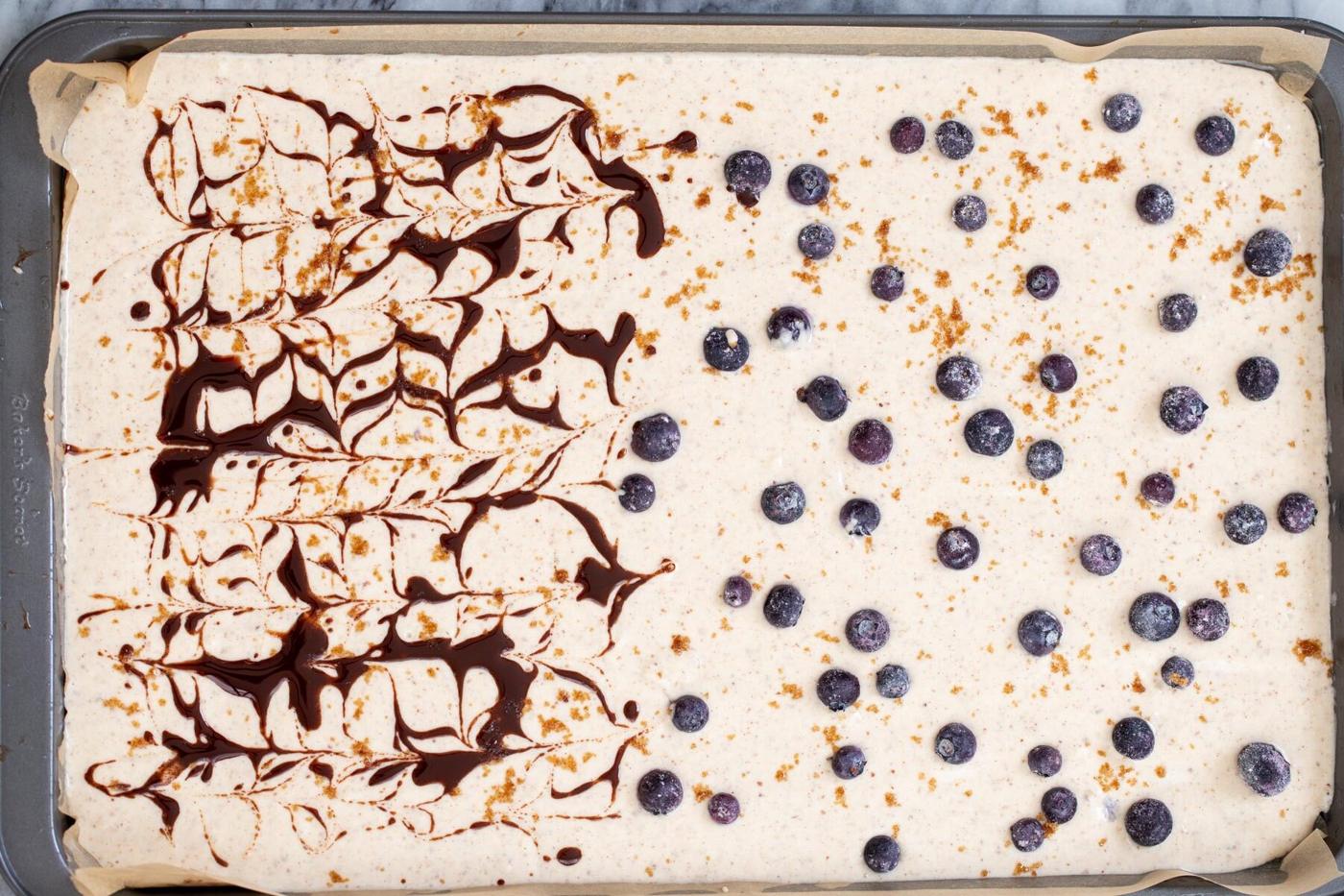 a sheet pan with pancake batter half topped with blueberries, half swirled with cinnamon syrup