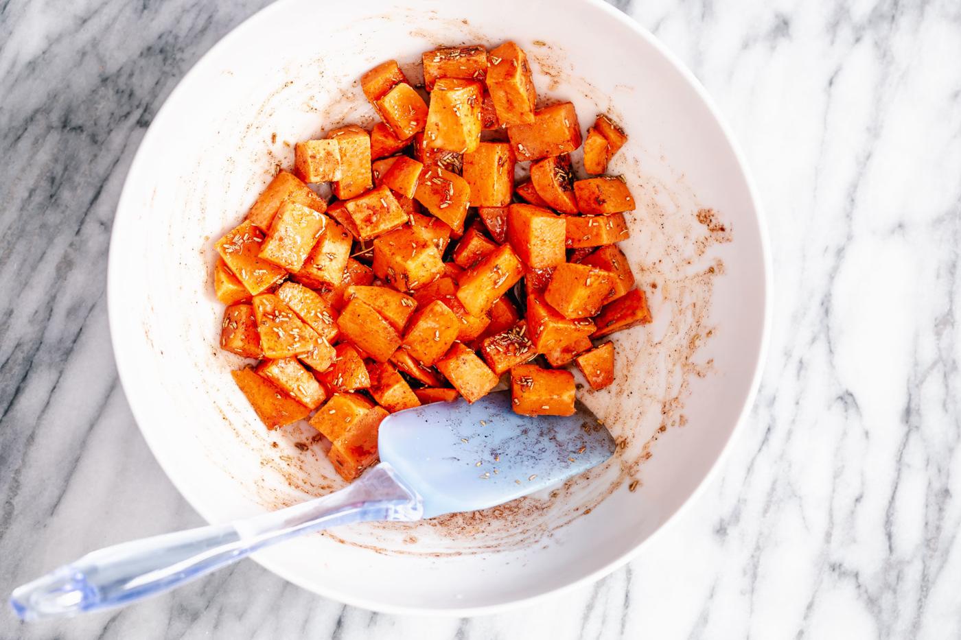 sweet potato cubes being tossed in a white bowl