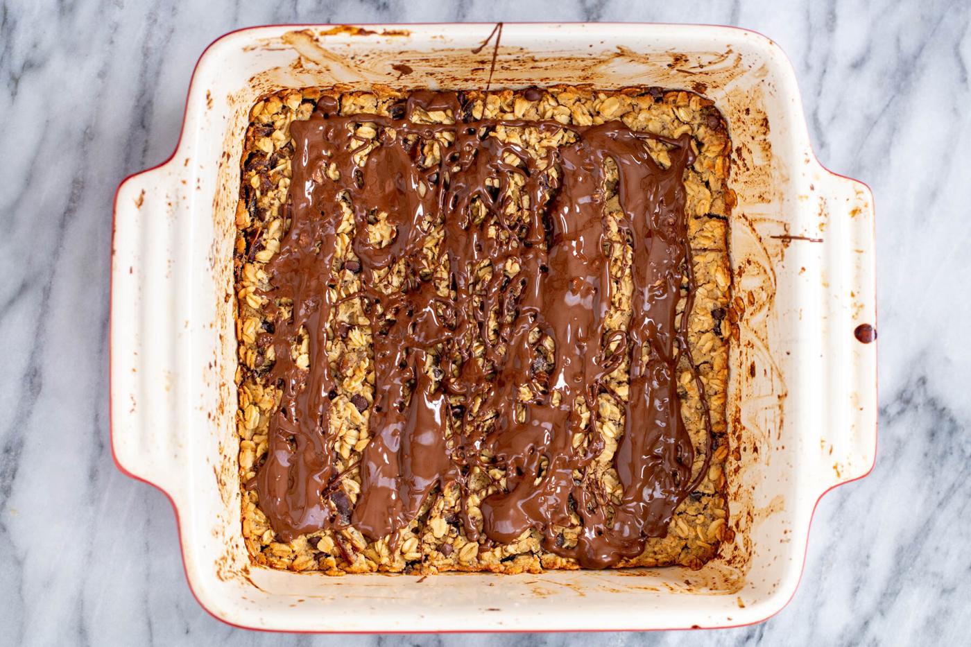 a casserole dish with peanut butter baked oatmeal drizzled with melted chocolate