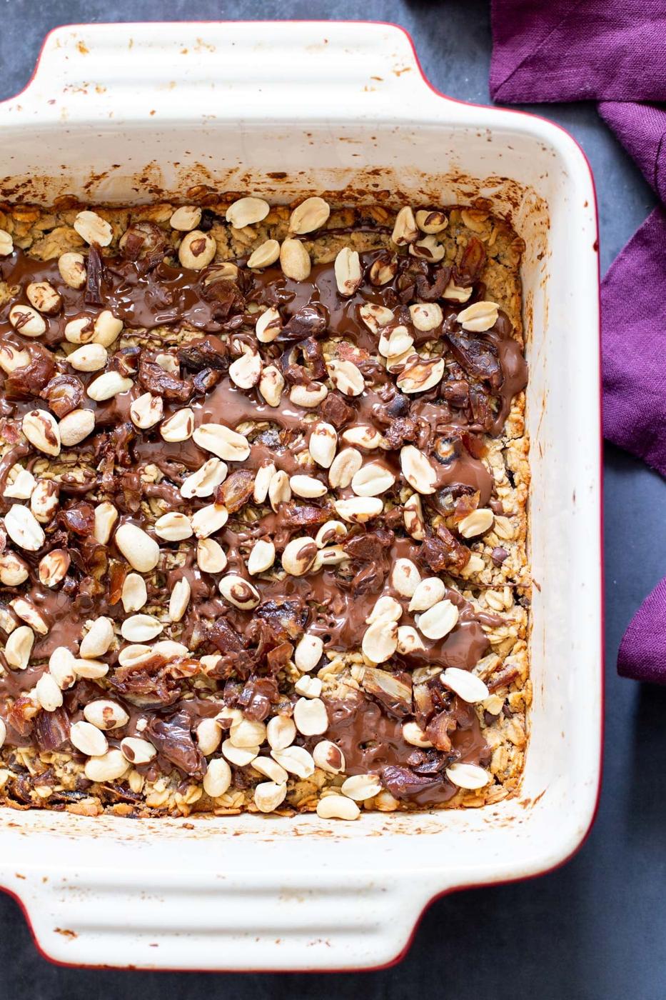 snickers baked oatmeal topped with peanuts and chocolate in a casserole dish