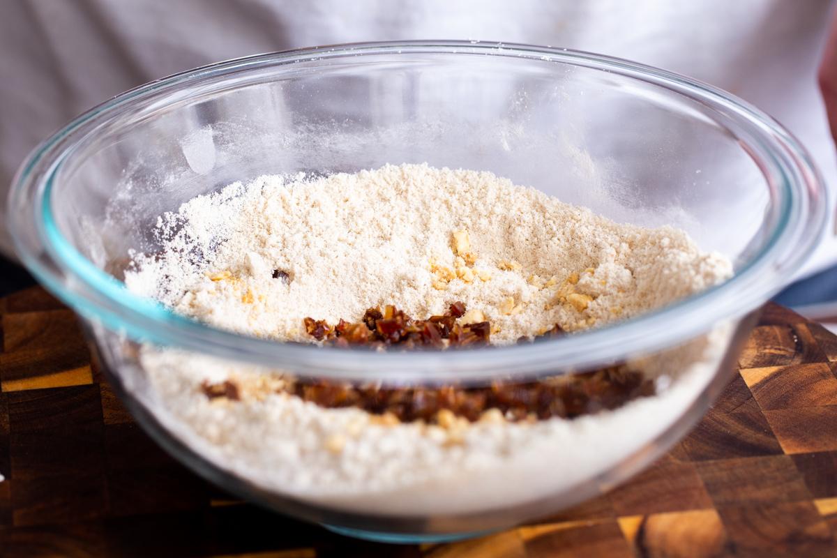 chopped dates and nuts being added to dry cookie ingredients in glass bowl