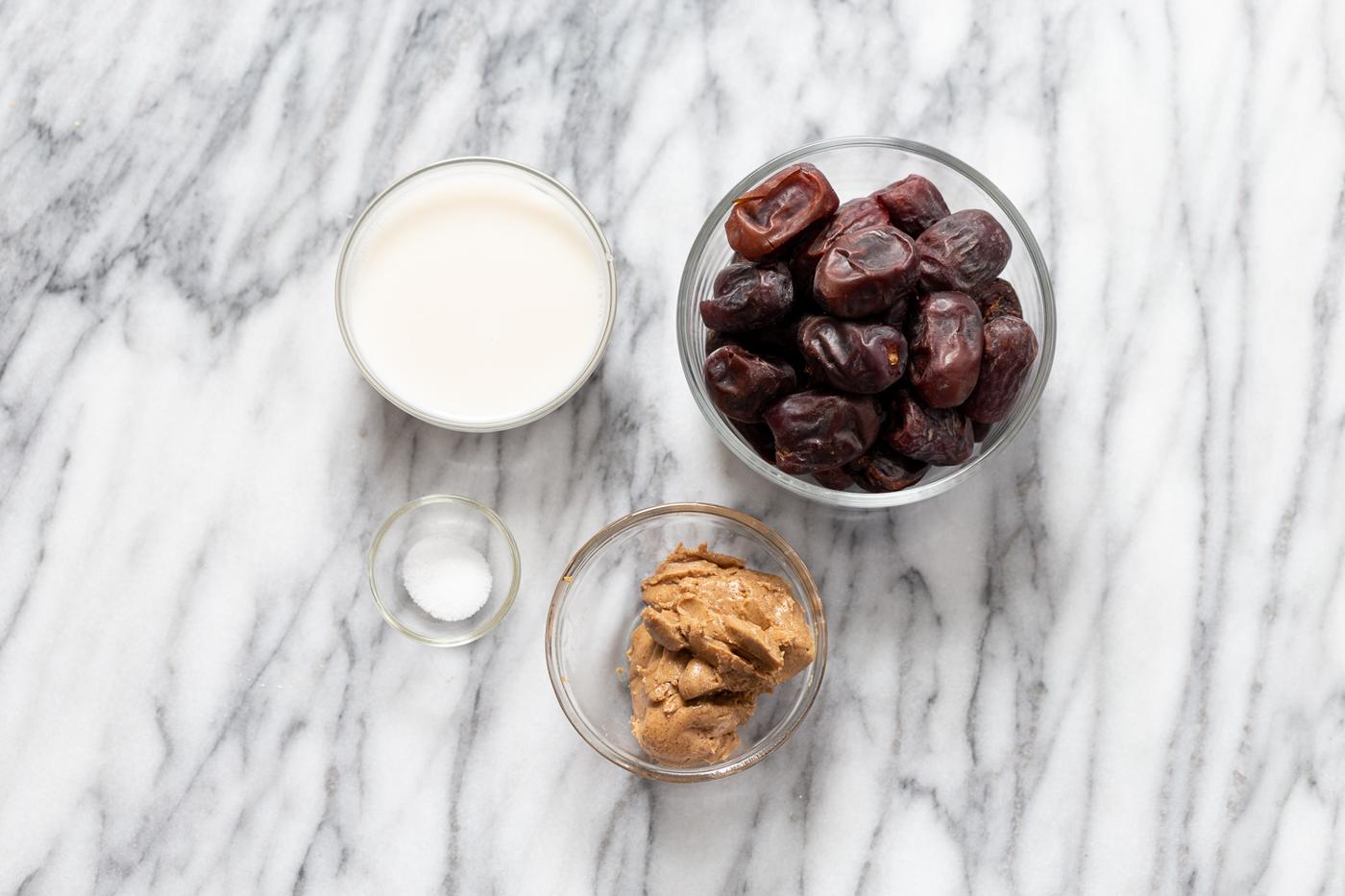 small glass dishes with plant based milk, dates, nut butter and salt on a kitchen counter