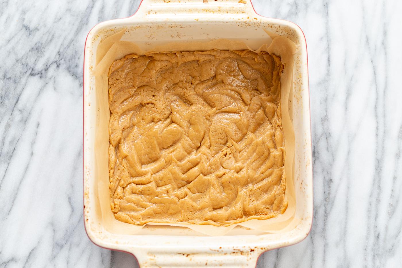 cookie base for vegan snickers snack bars recipe in a white baking dish