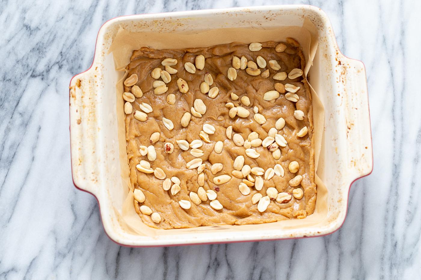peanuts being sprinkled on cookie base to make vegan snack bars