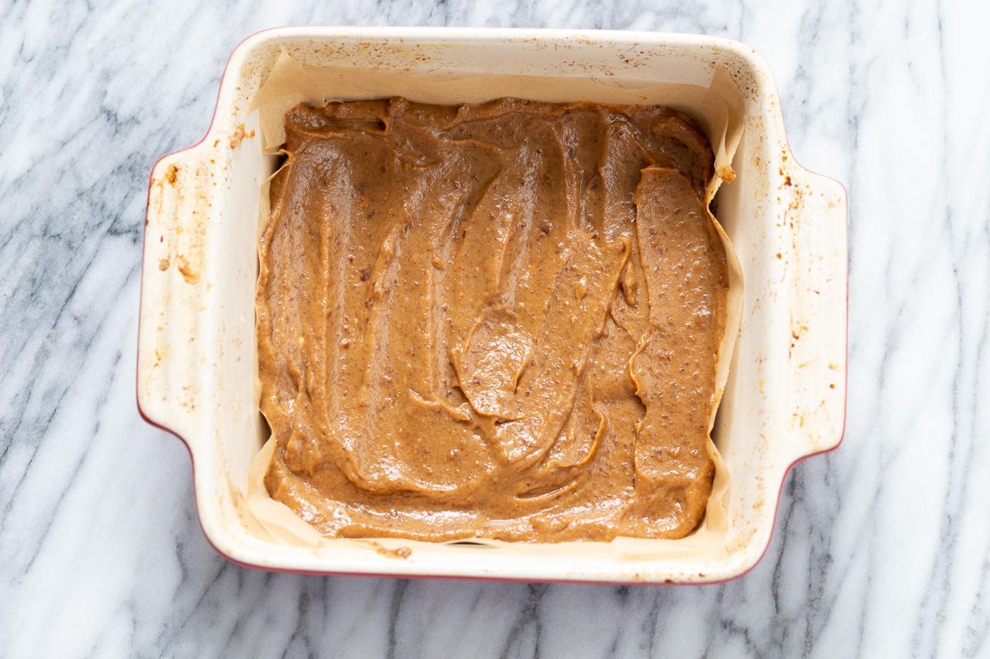 homemade vegan date caramel being spring onto cookie base to make vegan snickers snack bars recipe