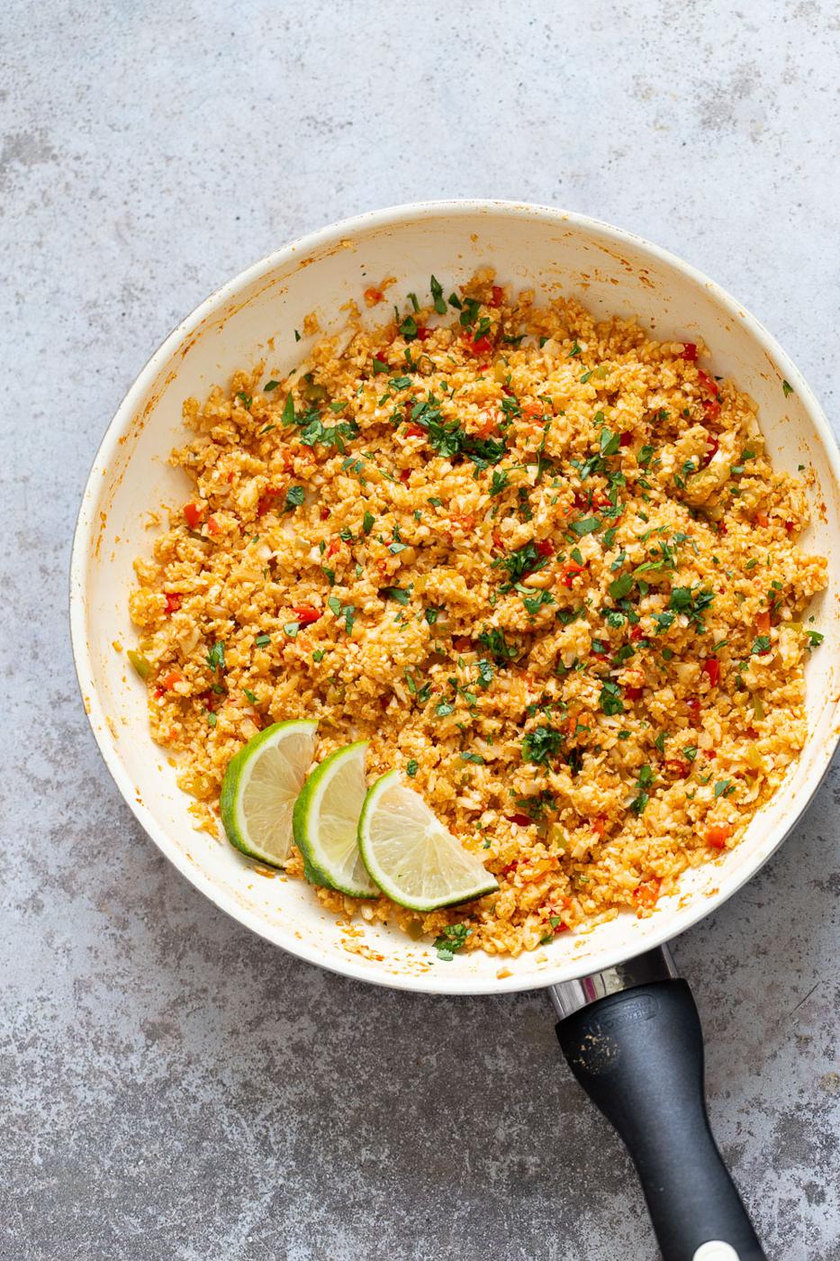 overhead hot of a pan with Spanish cauliflower rice decorated with cilantro and lime slices