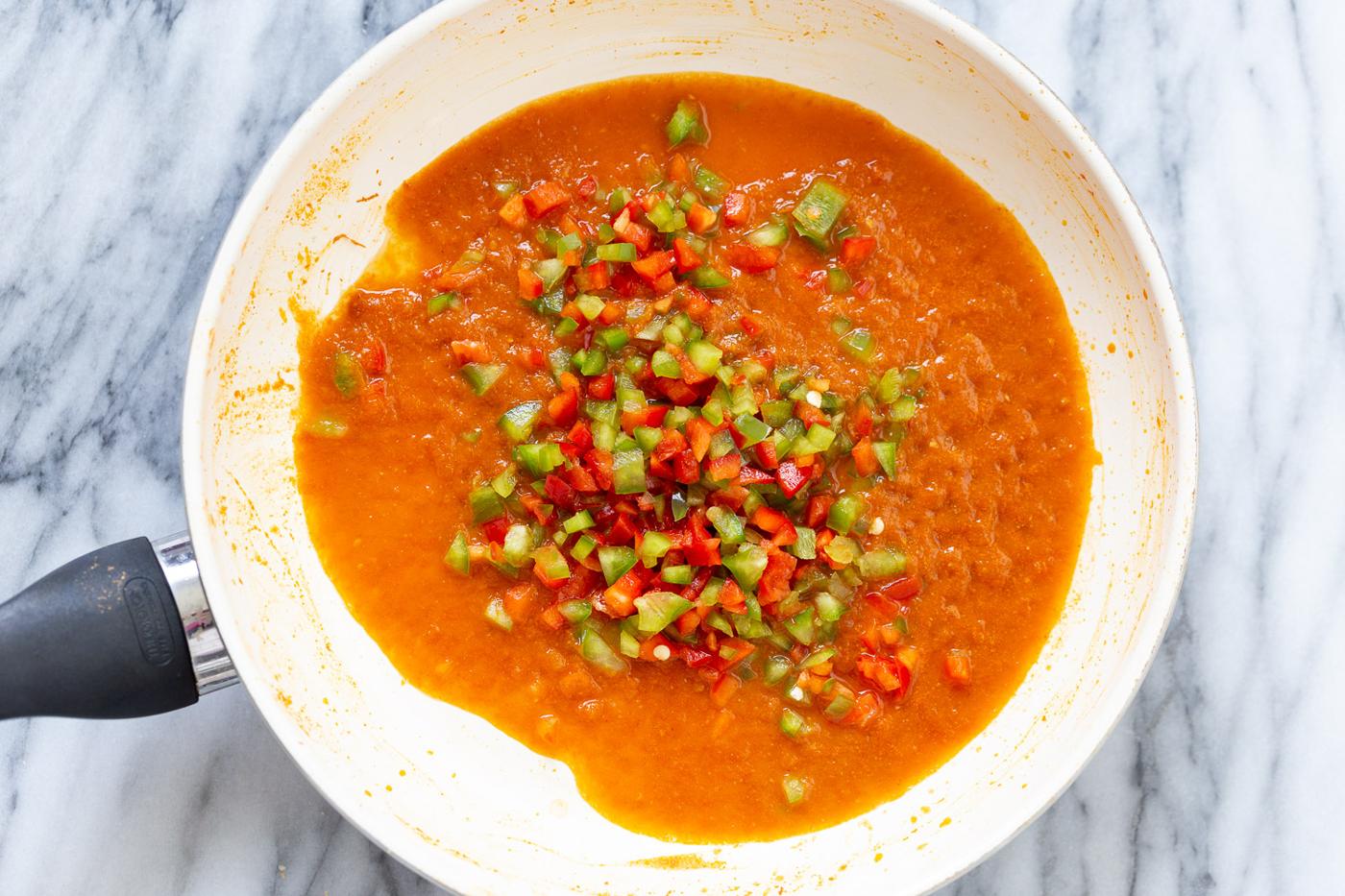overhead shot of a saucepan with tomato sauce and diced bell pepper for making Spanish cauliflower rice