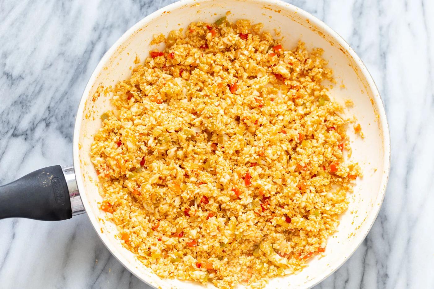 cauliflower rice being added to a saucepan with bell pepper sauce to make Spanish Cauliflower Rice