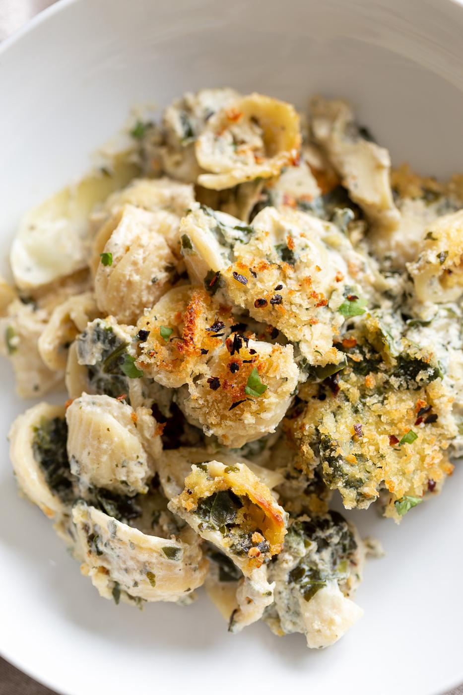 overhead shot of a plate of vegan spinach and artichoke pasta bake with breadcrumb topping