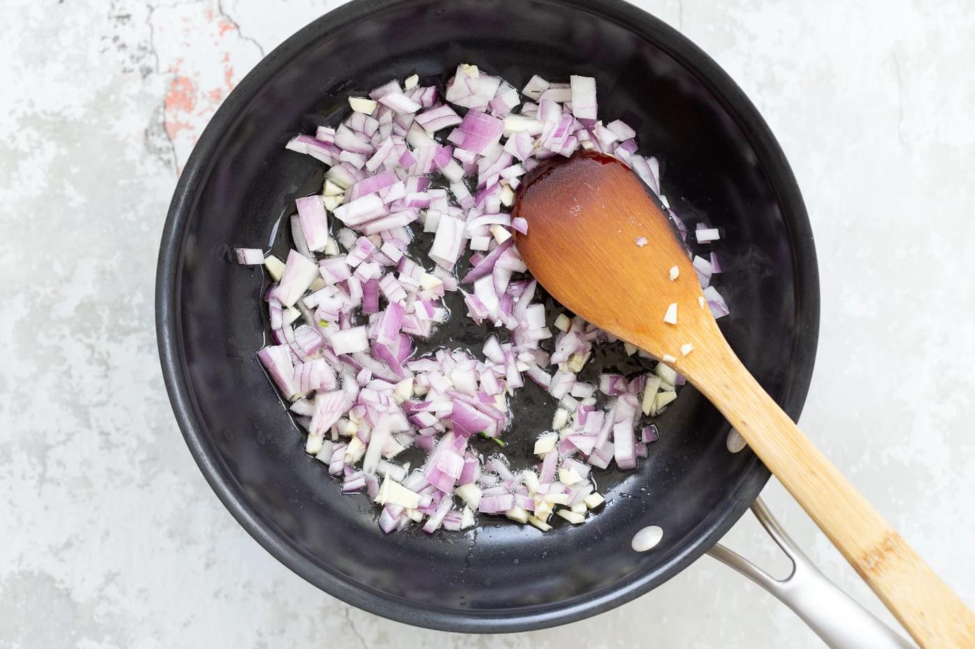 chopped red onions being sauteed in a black skillet