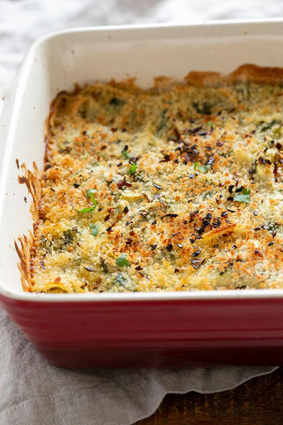 side view close up of a red casserole dish with creamy vegan artichoke spinach pasta bake