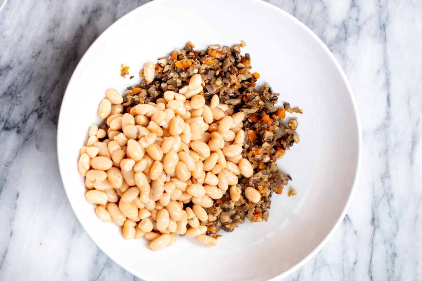 white beans being added to sauteed veggies in a pan