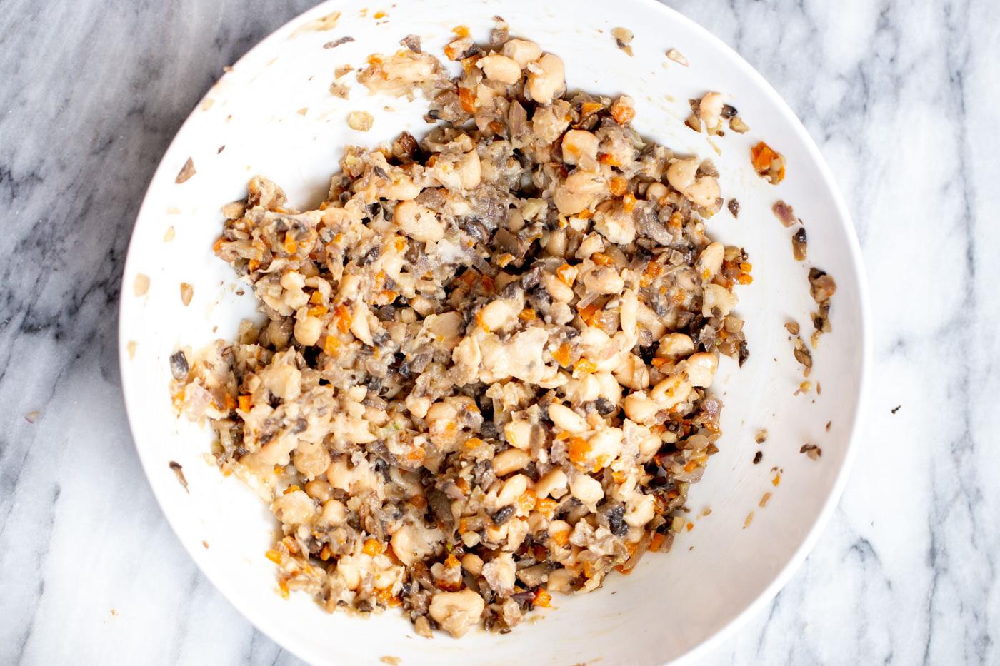 white beans being mashed into veggies in a sauteeing pan