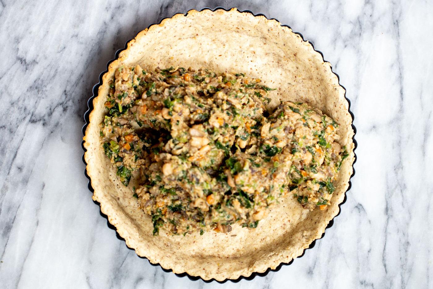 vegan spinach mushroom filling being added to savory pre-baked crust