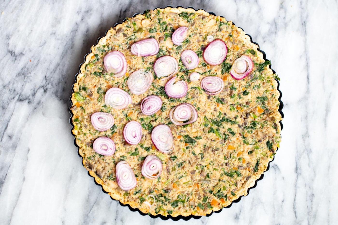 vegan mushroom tart being topped with onion slices