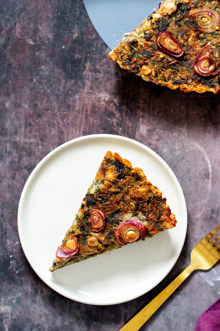 a slice of vegan spinach mushroom tart on a white plate with a fork on the side