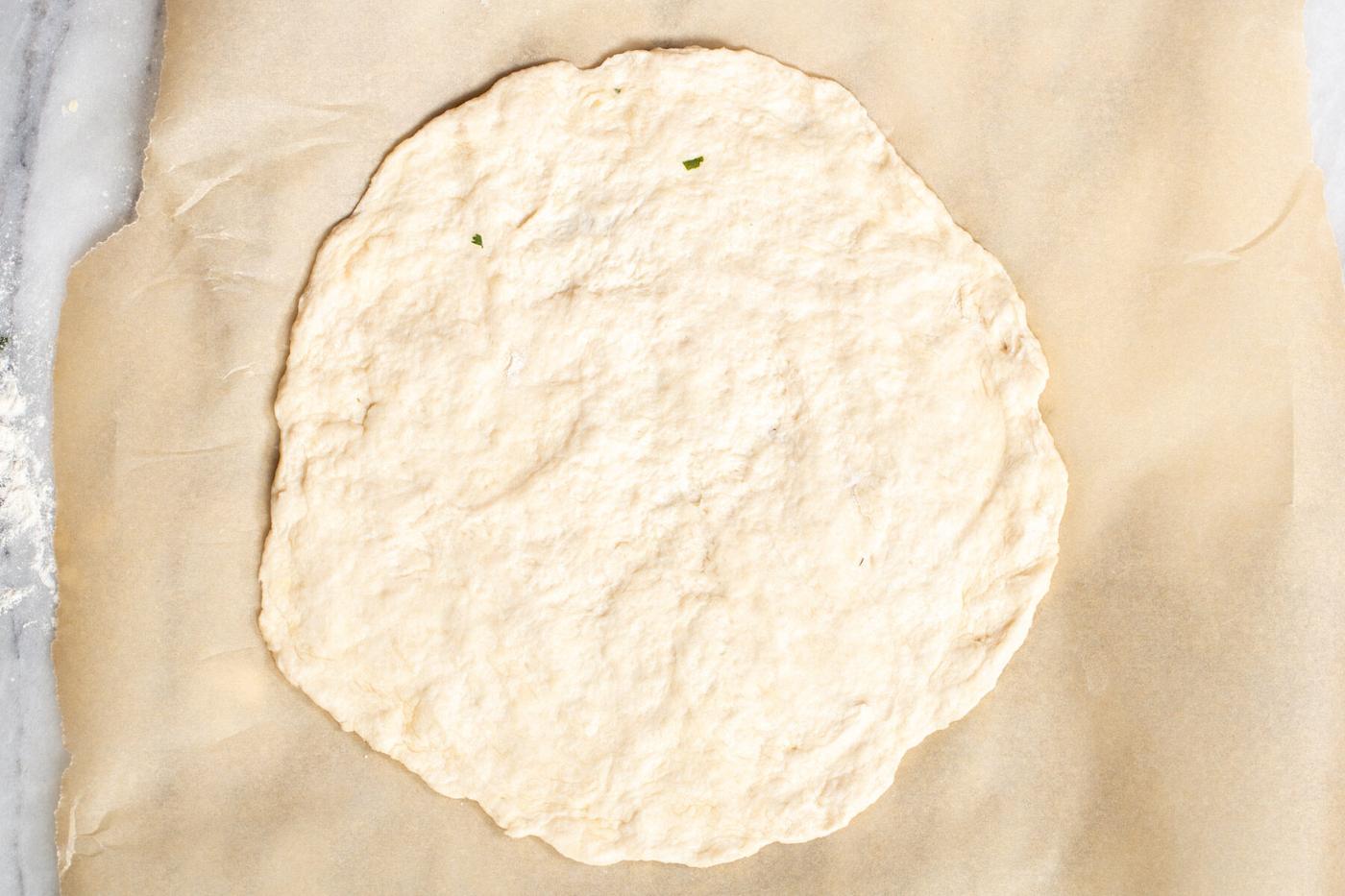 naan dough being rolled out on a sheet of parchment paper