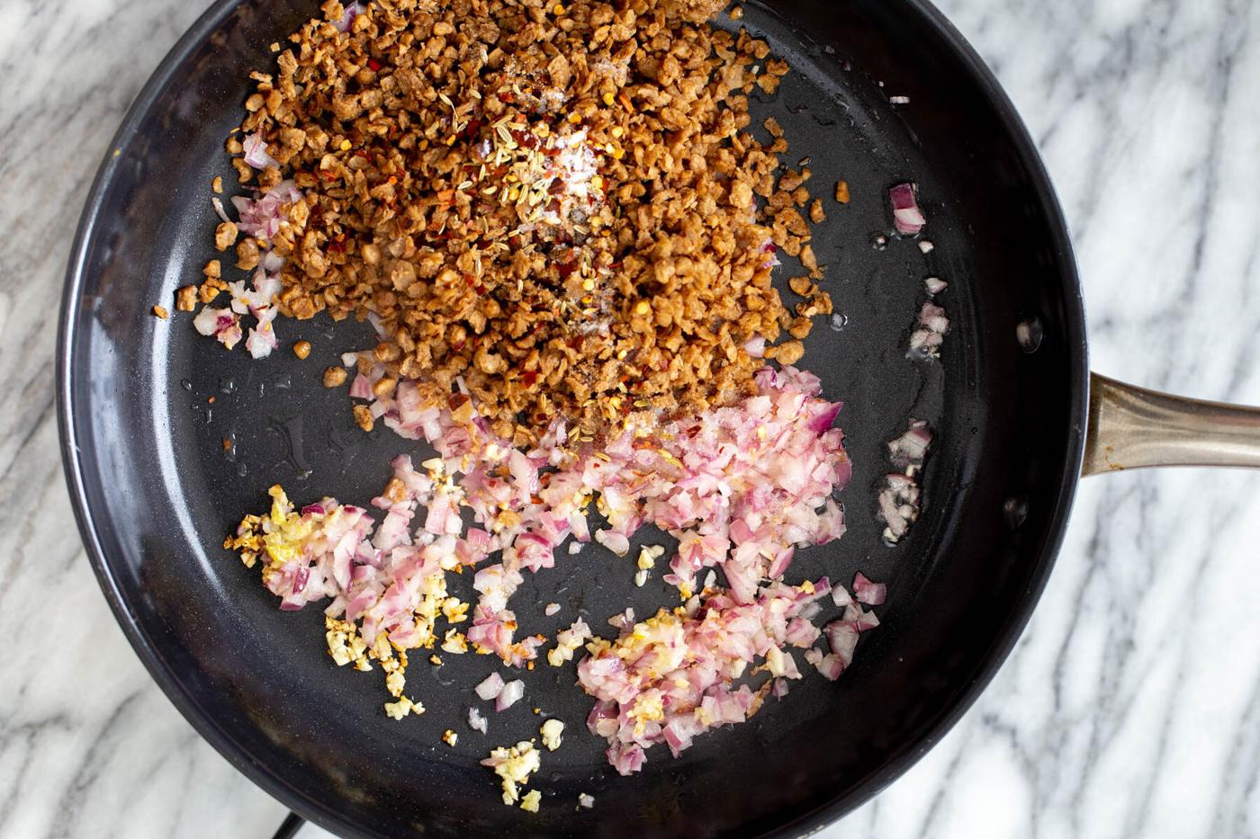 veggie crumbles being added to sauteed garlic and onions