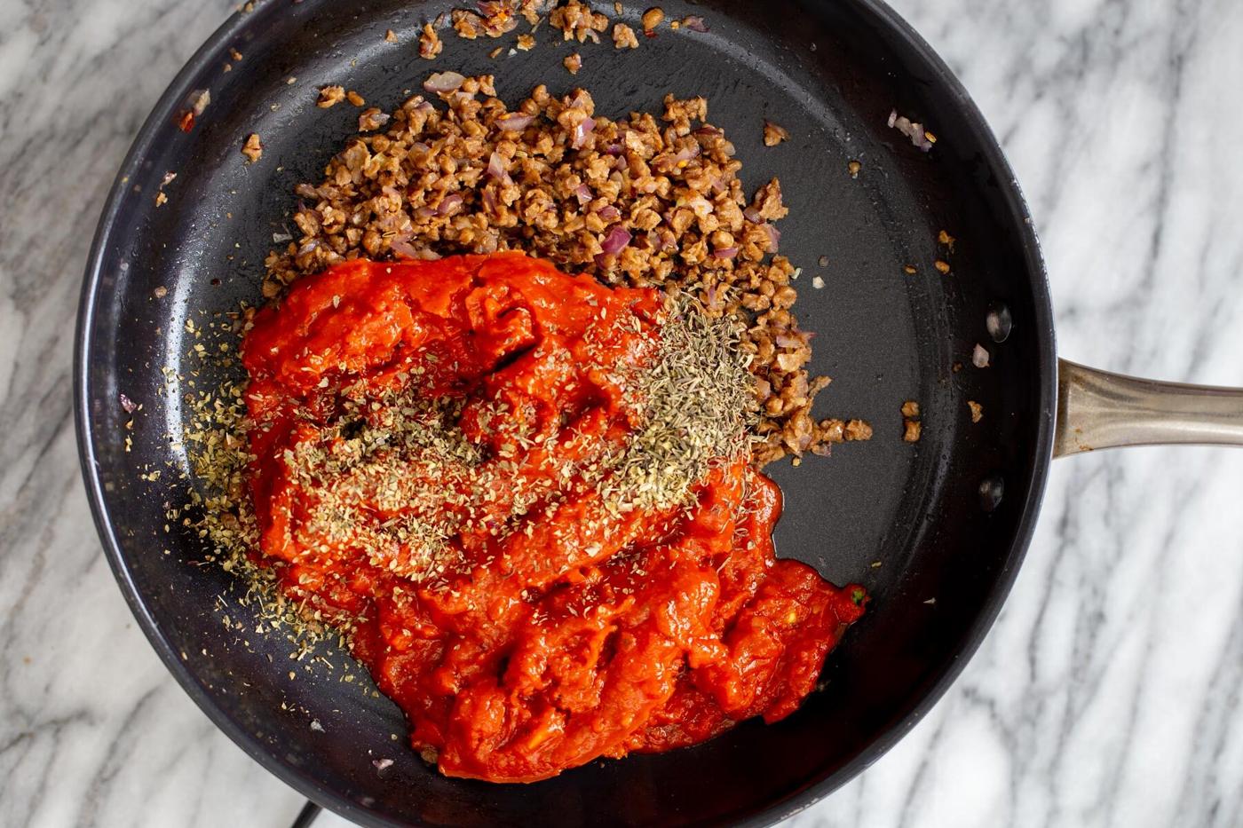 tomato sauce being added to a skillet with vegan meat crumbles