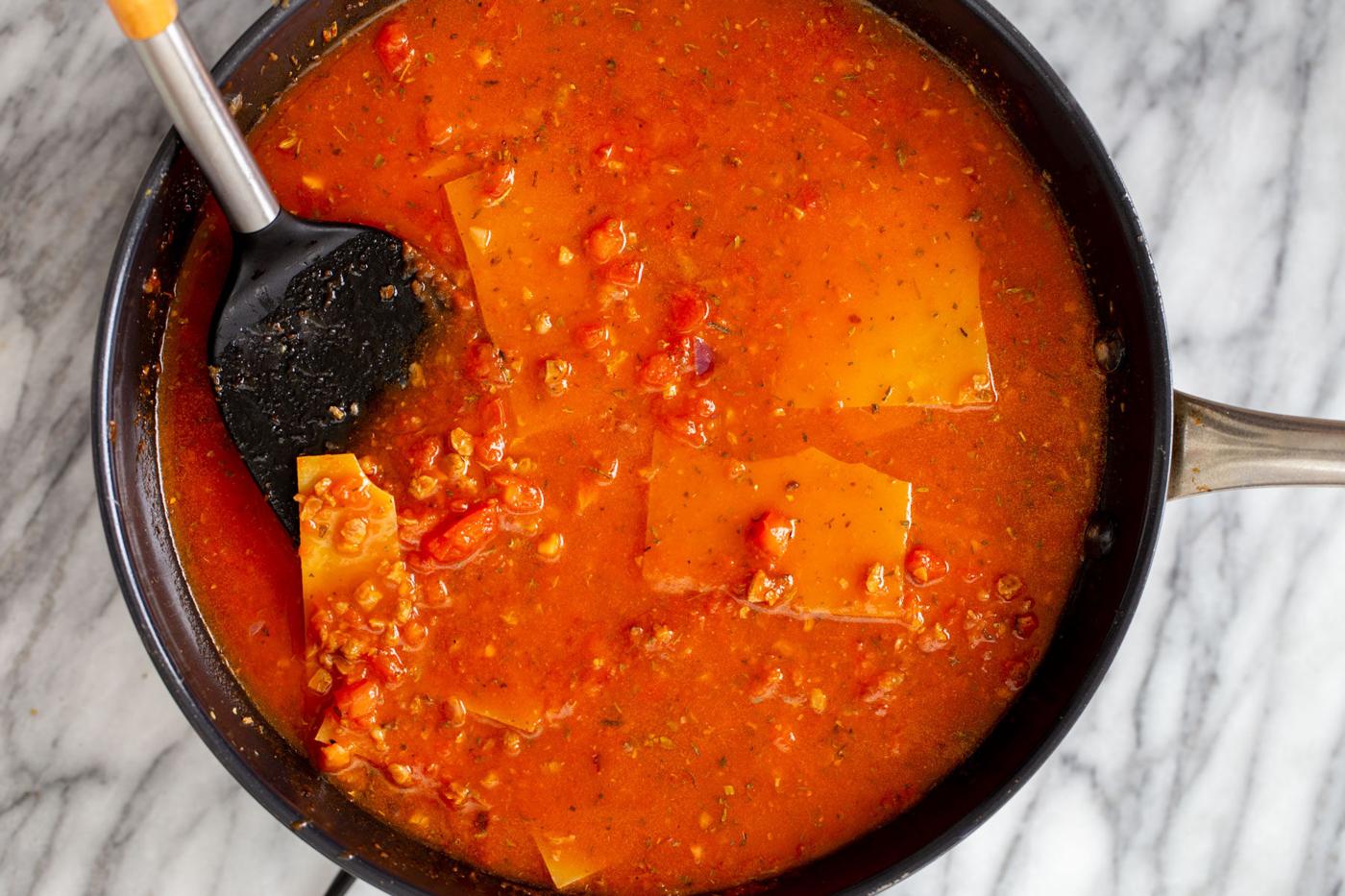 broked lasagna noodles being added to marinara sauce in a skillet