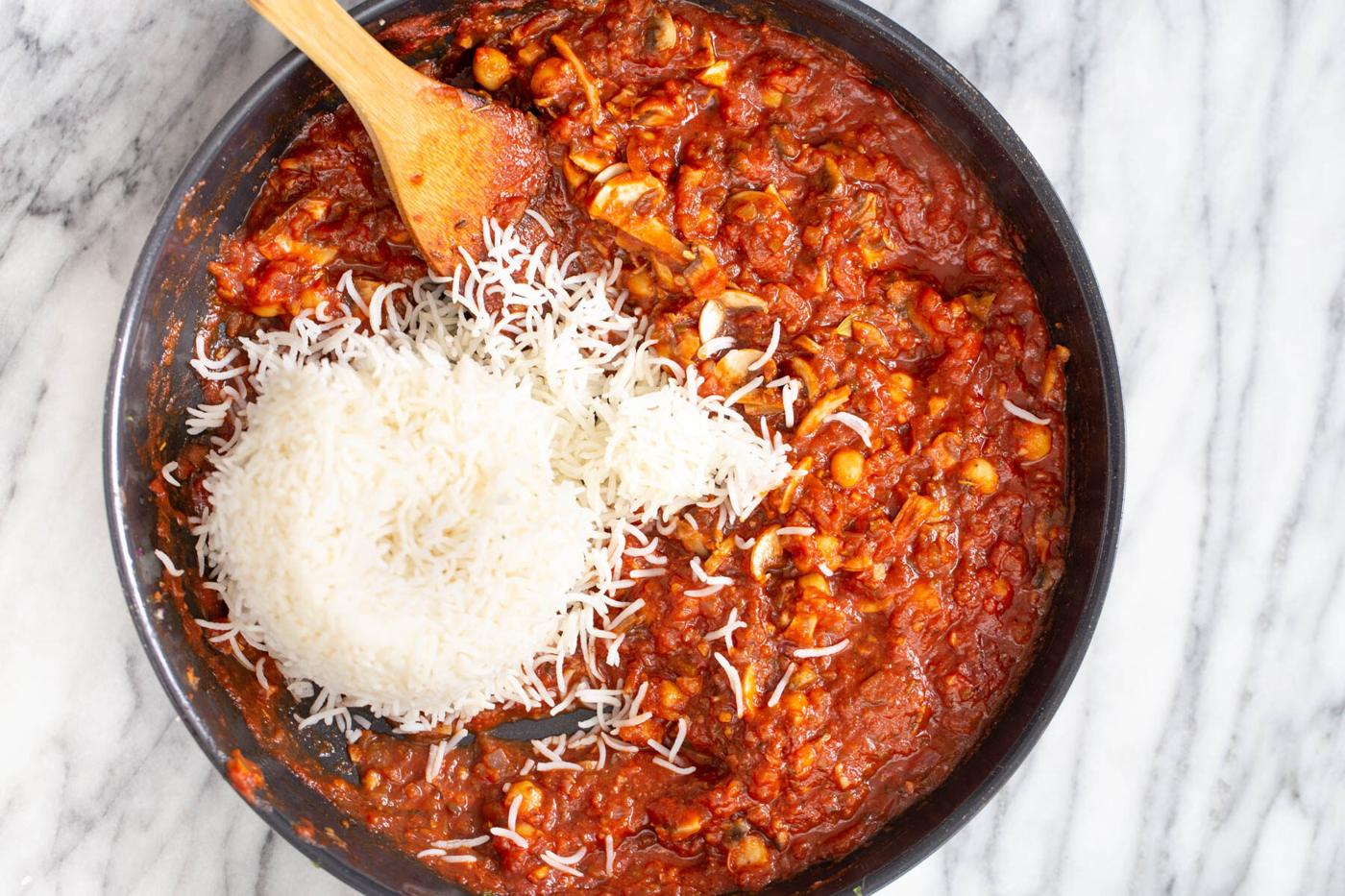 cooked rice being added to tomato sauce to make stuffed bell peppers