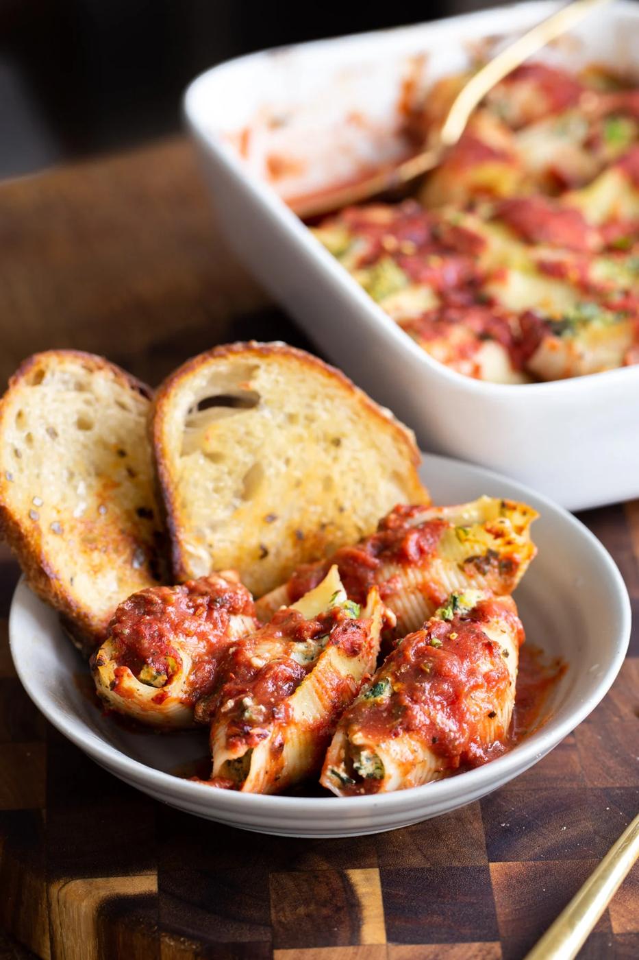 a serving of vegan stuffed shells in a white bowl served with two slices of bread
