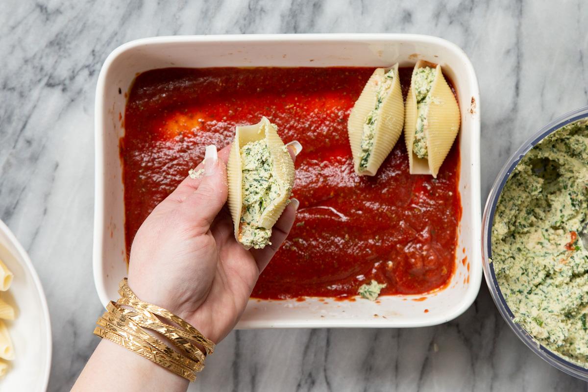 stuffed shells being placed in a casserole dish with marinara sauce