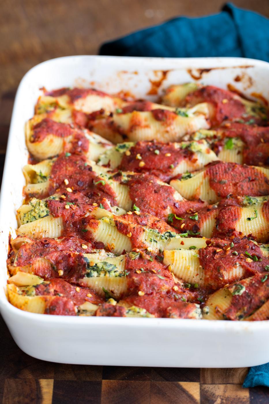 a white casserole dish with vegan stuffed shells sprinkled with chili flakes
