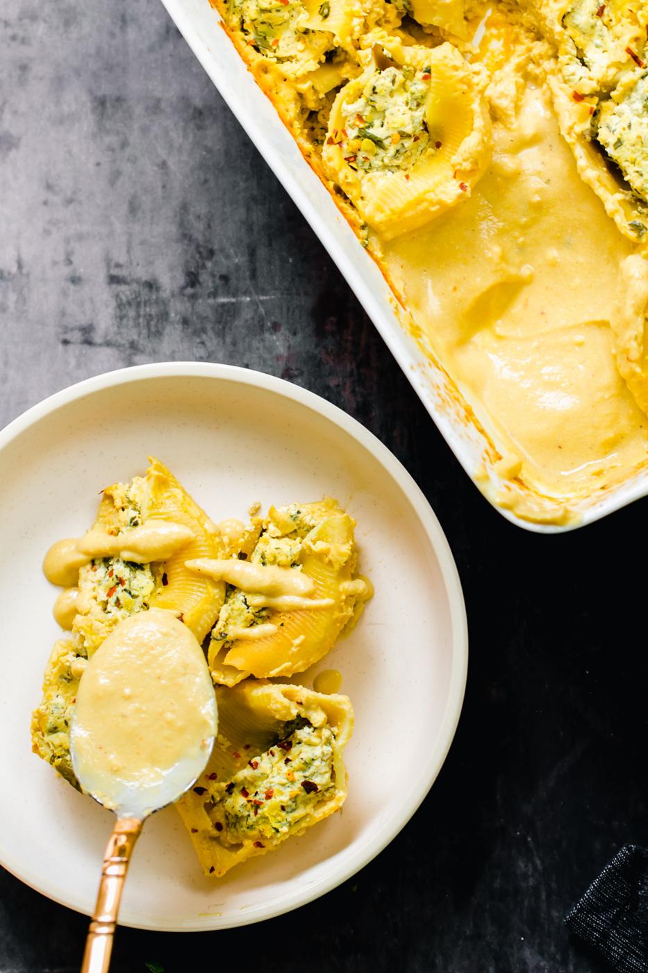 butternut squash alfredo sauce being drizzled on vegan stuffed shells on a white plate