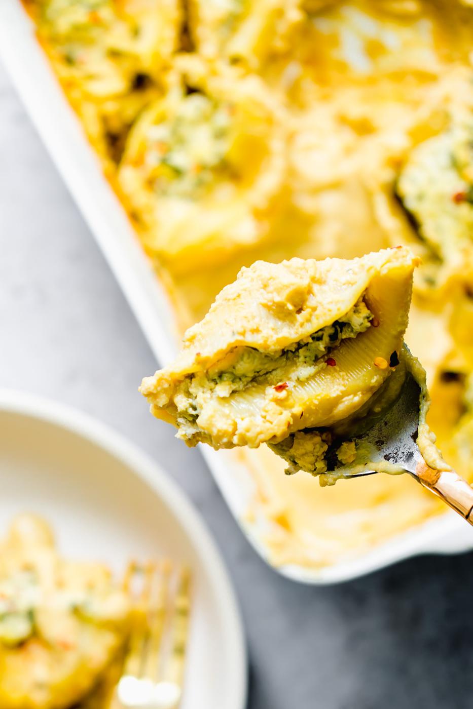 a spoon holding a vegan stuffed shell filled with tofu ricotta